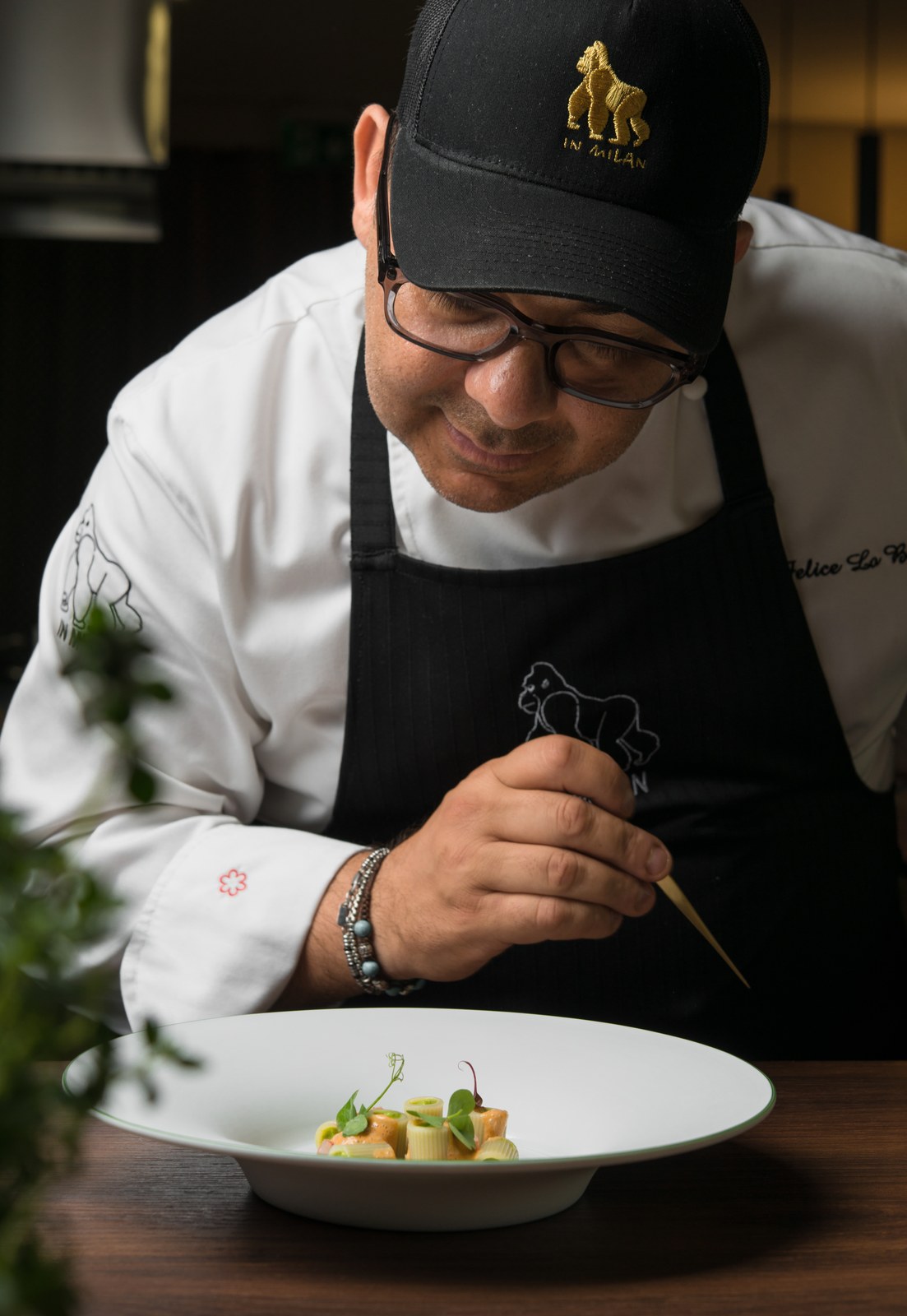 Felix Lo Basso completa un piatto con una pinzetta, indossando la giacca da chef e un grembiule nero